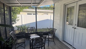 Eine überdachte Terrasse mit Tisch, Stühlen, Blumentöpfen und Blick auf einen Garten.