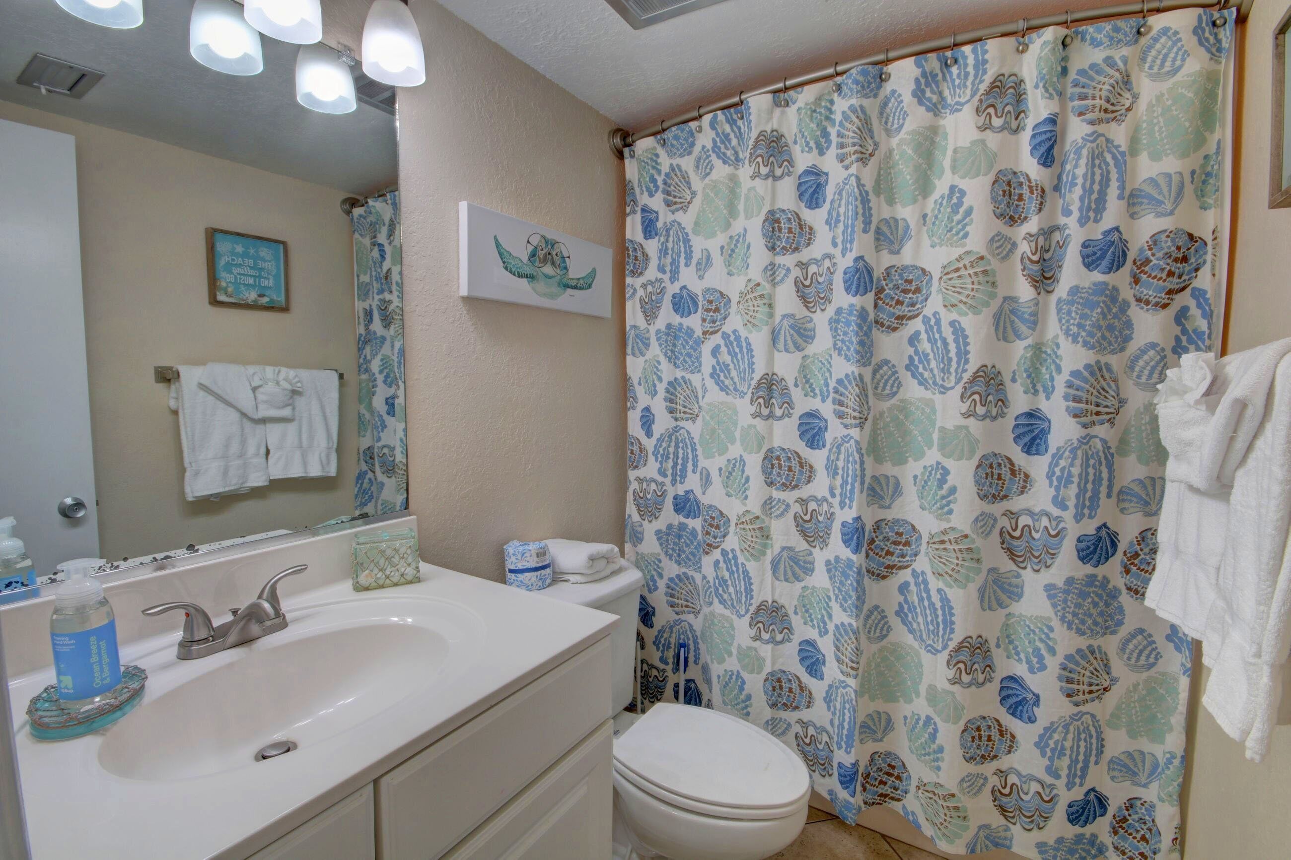 A bathroom with a white sink, a toilet, and a shower curtain with a shell pattern.