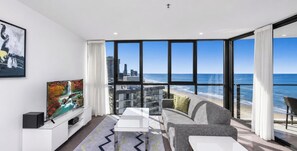 A modern living room with a large window overlooking a beach and cityscape. - Lvl 23 |  Unbearable Ocean View 1BR | 50m to beach (Surfers Paradise)