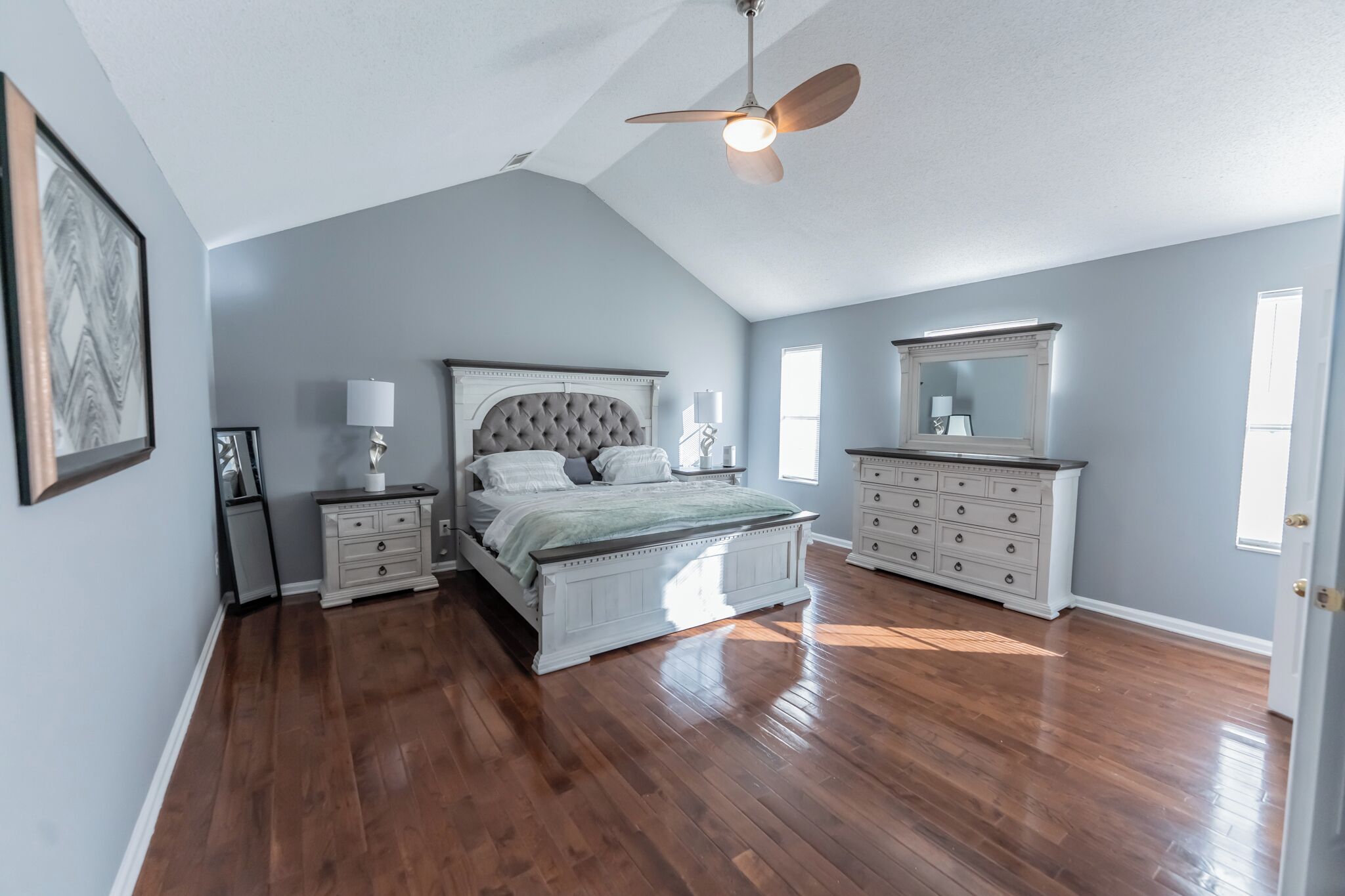 Een slaapkamer met een groot bed, een plafondventilator, een dressoir en een spiegel.