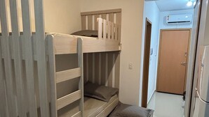 A compact bedroom with a bunk bed, a small bedside table, and a door leading to a hallway.