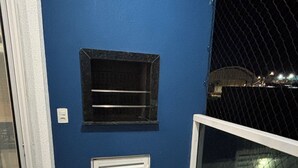 A balcony with a blue wall, a black shelf, a white vent, and a glass door.