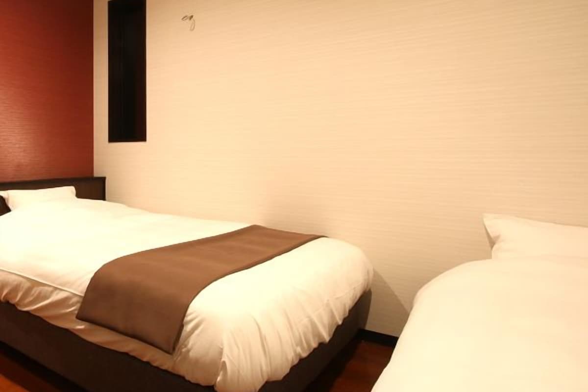 Habitación de hotel con dos camas, suelo de madera y aire acondicionado de pared.