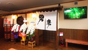 A traditional Japanese restaurant interior with wooden flooring, a TV mounted on the wall, and a fire extinguisher. - Hitoyoshi Onsen Oga no Yado (Hitoyoshi)