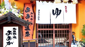 A traditional Japanese building with a wooden facade, a large wooden sign with Japanese characters, and a white banner with red characters.
