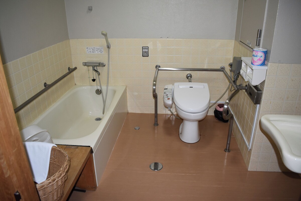 Ein Badezimmer mit Badewanne, Toilette und Waschbecken, ausgestattet mit Haltegriffen und einem Händetrockner.