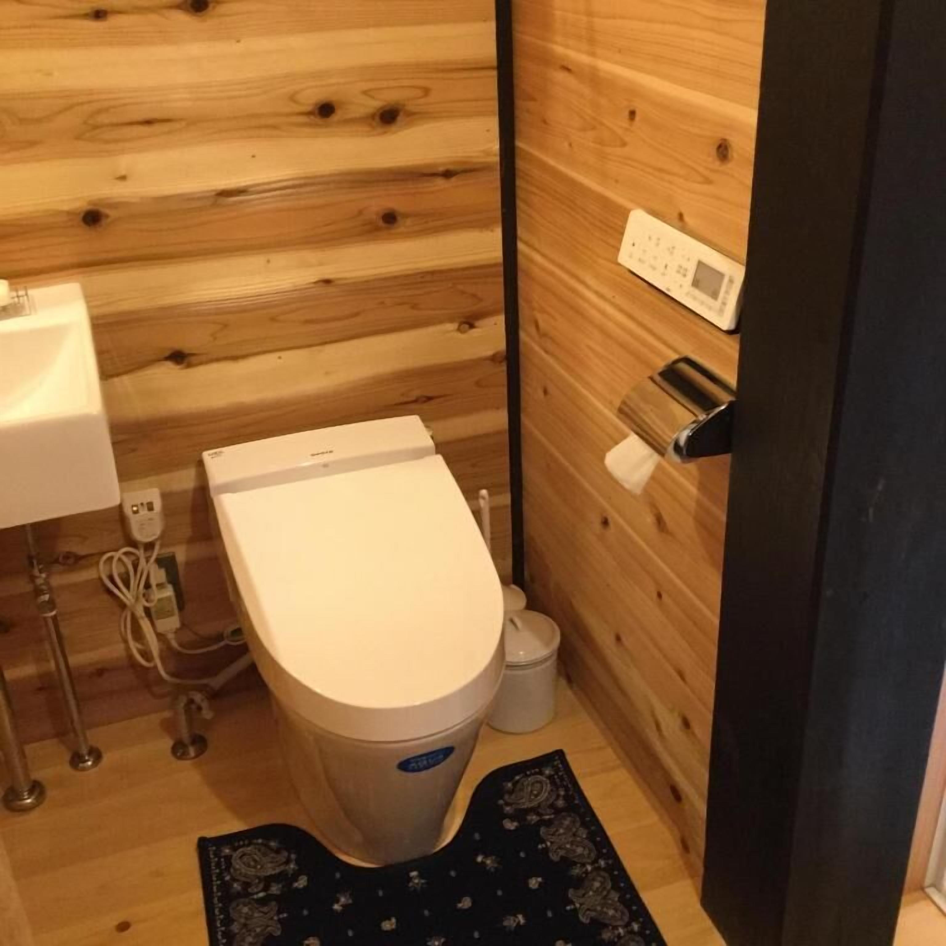 A small, compact bathroom with a wooden wall, a white toilet, a sink, and a small trash bin.