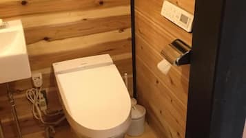 A small, compact bathroom with a wooden wall, a white toilet, a sink, and a small trash bin.