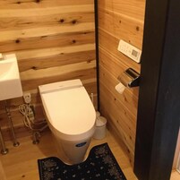 Un baño pequeño y compacto con pared de madera, inodoro blanco, lavamanos y un cubo de basura pequeño.