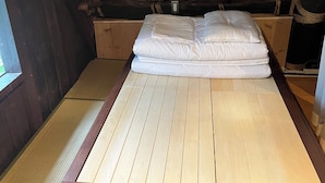 Una cama con estructura de madera y ropa blanca en una habitación con techo rústico cubierto de cuerda.