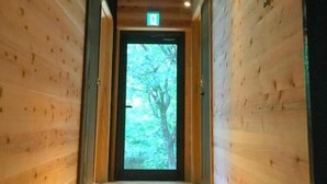 Pasillo interior de madera que conduce a una puerta con vistas a árboles.