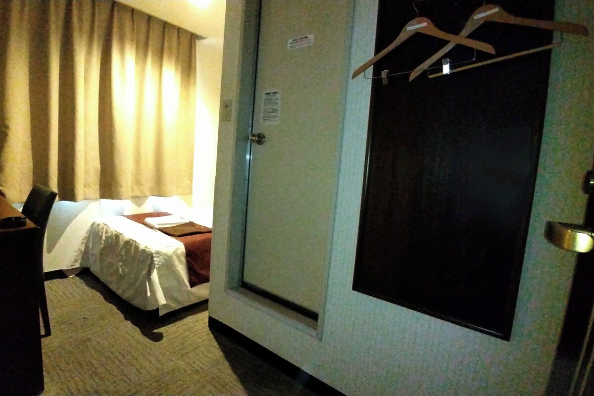 A hotel room with a bed, a desk with a computer, a chair, and a door with a coat rack.