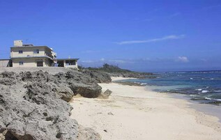 Una propiedad frente a la playa con un edificio grande que domina el océano, una playa de arena y terreno rocoso.