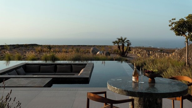 Ein Infinity-Pool mit moderner Außensitzgruppe, einem Tisch mit Flasche und Glas sowie Blick aufs Meer.