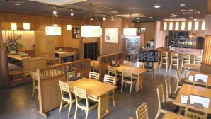 L’intérieur d’un restaurant, avec des meubles en bois, des luminaires suspendus et un coin bar.
