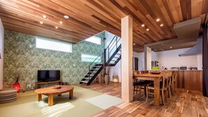 A spacious living area with a wooden ceiling, a flat-screen TV, a wooden dining table, and a kitchen area with modern appliances. - Kawaguchiko Villa FJ Resort (Fujikawaguchiko)