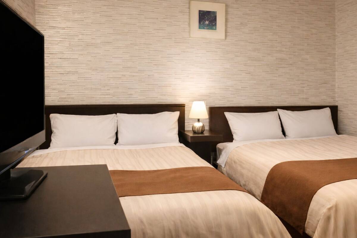 Hotelkamer met twee bedden, een televisie, een nachtkastje met lamp en een schilderij aan de muur.