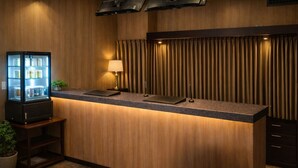 Un comptoir d’accueil d’hôtel avec un mur recouvert de panneaux en bois, une vitrine, une lampe de bureau et une plante en pot.
