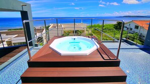 Un jacuzzi en una terraza de madera con vista al océano y edificios al fondo.