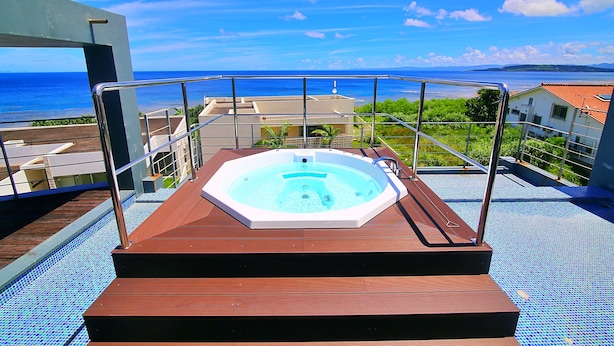 Een hottub op een houten terras met uitzicht op zee en gebouwen op de achtergrond.