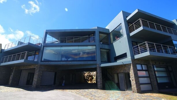 Un edificio moderno de varios pisos con fachada de vidrio, balcones y base de piedra.