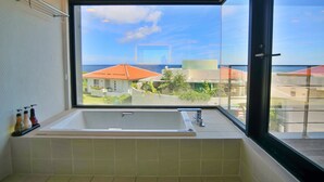 Un baño con un ventanal grande, una bañera y vistas a edificios y al mar.
