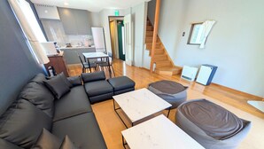 A modern living room with a sectional sofa, two white marble coffee tables, and a round bean bag. A staircase is visible in the background. - Nasu Kogen Rental Cottage Yellow Base (Nasushiobara)