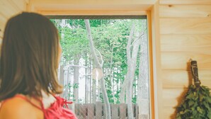 A person standing in a room with a window overlooking a wooden deck and trees. - Nasu Kogen Rental Cottage Yellow Base (Nasushiobara)