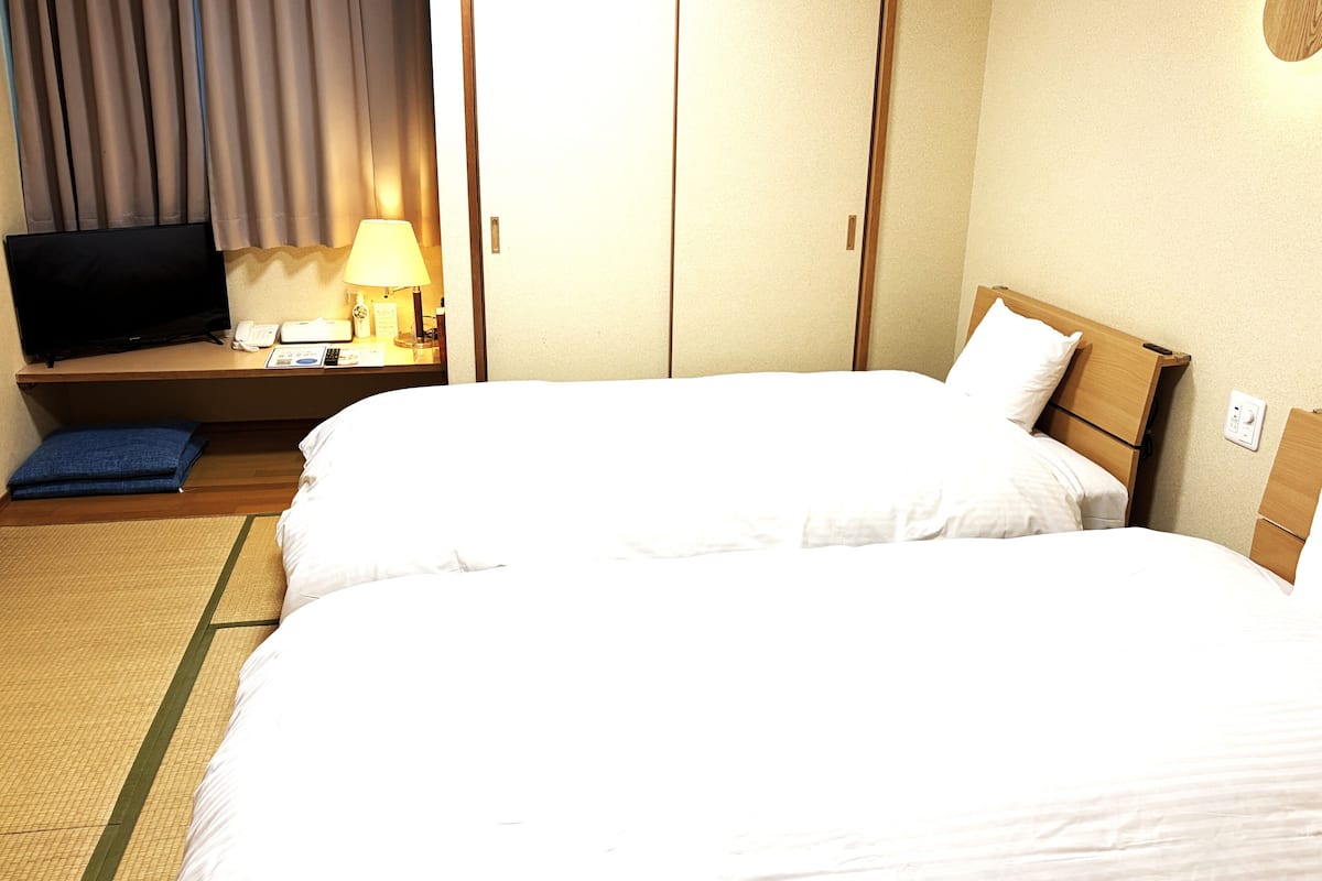 Ein Hotelzimmer mit zwei Betten, einem Fernseher, einer Lampe und einem Schreibtisch mit Telefon und Notizblock.