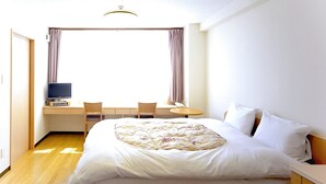 Ein Hotelzimmer mit einem Bett, einem Schreibtisch mit Computer, einem Stuhl und einem Fenster mit Vorhängen.