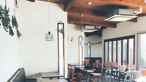 Ein Restaurant mit Holztischen und -stühlen, einer schwarzen Couch und großen Fenstern.