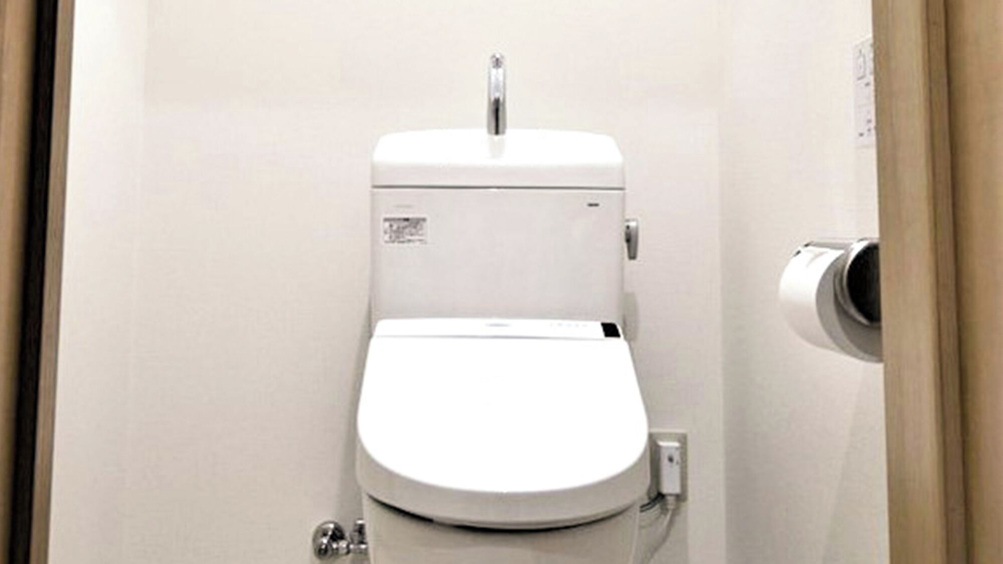 A white toilet with a flush handle and a paper towel dispenser.
