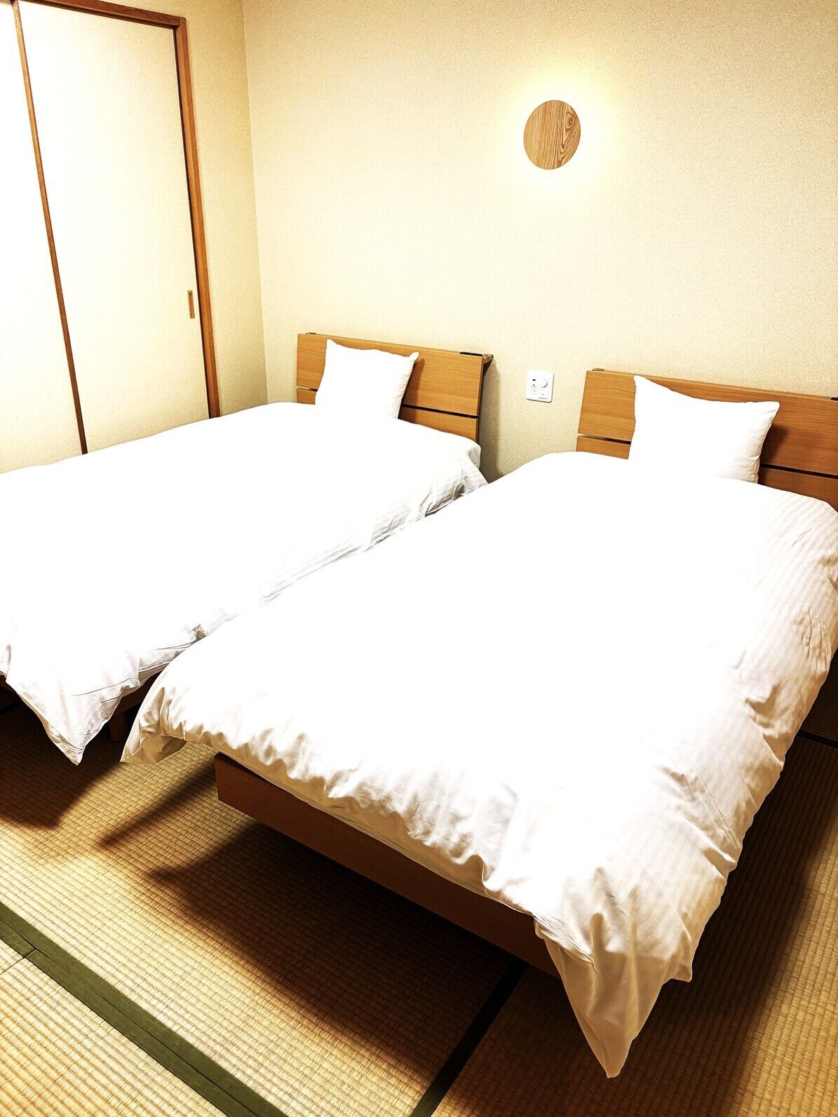 Ein Hotelzimmer mit zwei Betten, einem Holzkopfstück, einer Wandleuchte und einer Tür.