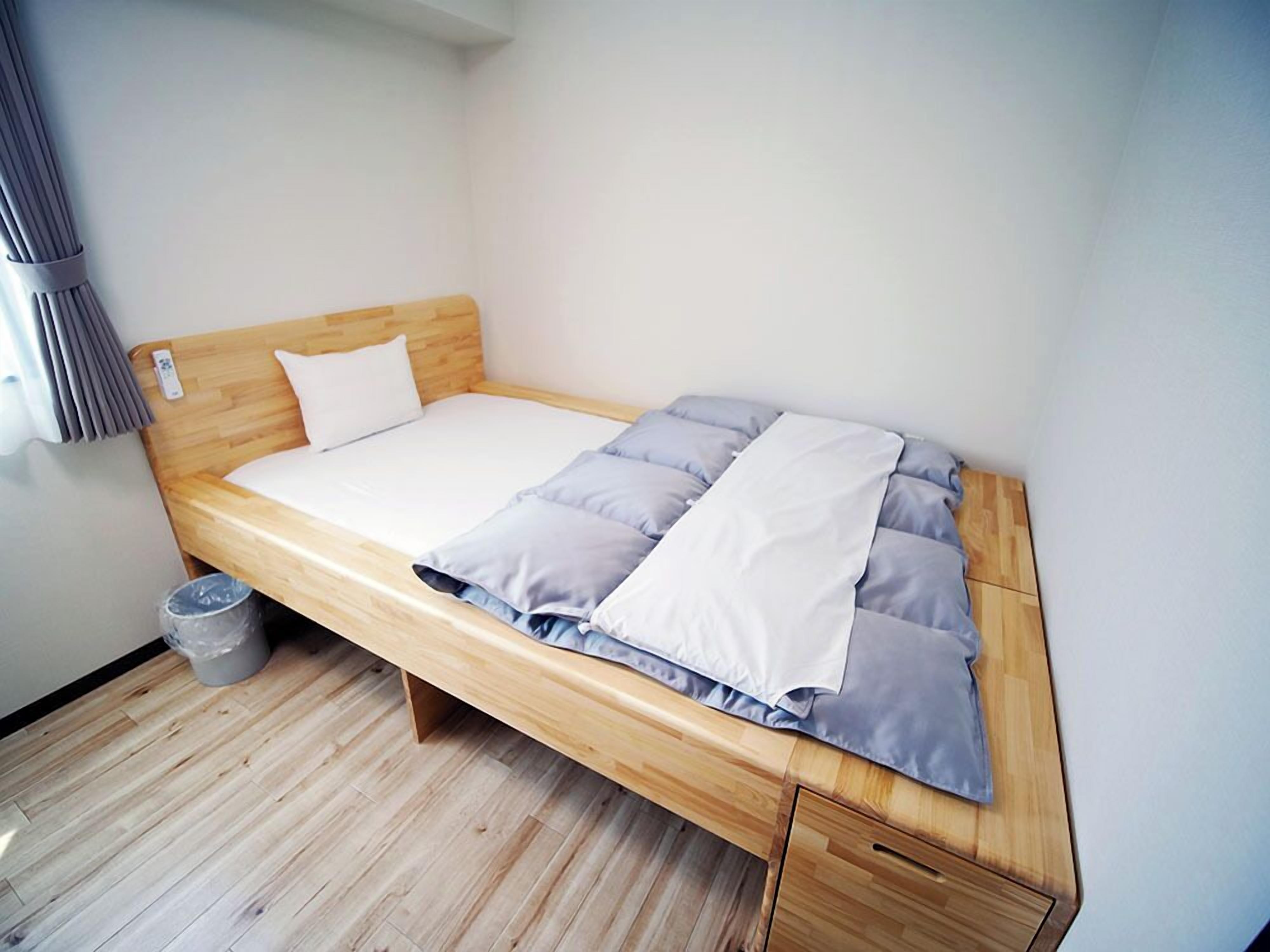 Ein Einzelbett mit Holzrahmen, Bettwäsche in Grau und Weiß, und ein kleiner Mülleimer daneben.