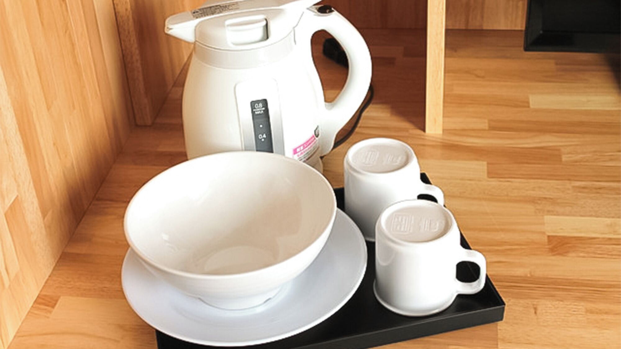 Uma área de cozinha com uma chaleira branca, uma tigela branca e duas xícaras brancas sobre um suporte preto.