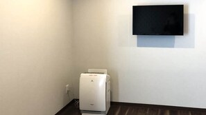 A room with a white wall, a flat-screen TV mounted above a white printer, and a dark wooden floor. - Sparky's House / House II (Naoshima)
