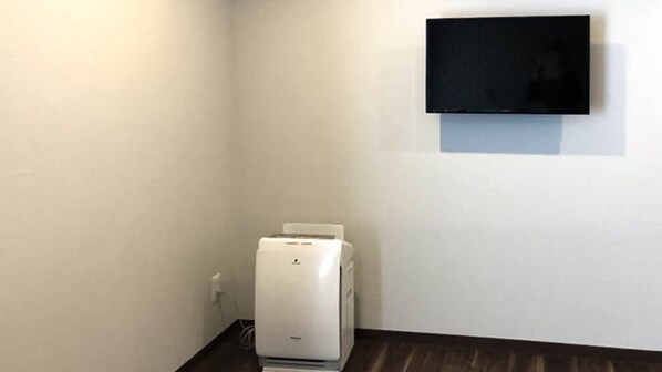 A room with a white wall, a flat-screen TV mounted above a white printer, and a dark wooden floor. - Sparky's House / House II (Naoshima)