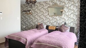 A bedroom with two beds, floral wallpaper, a mirror, and a chandelier. - Sparky's House / House II (Naoshima)
