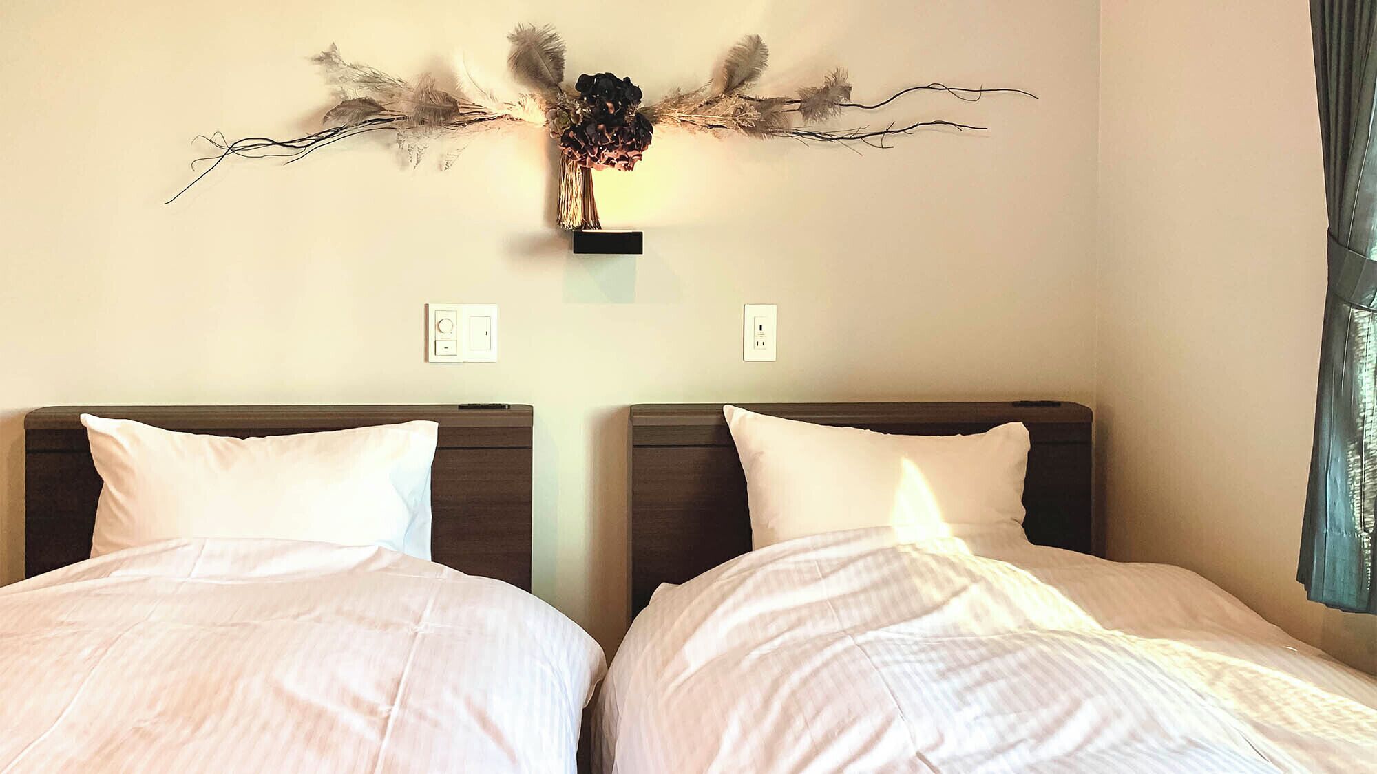 A hotel room with two beds, each with white bedding and dark headboards. There is a wall-mounted decorative piece above the beds.