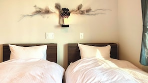 A hotel room with two beds, each with white bedding and dark headboards. There is a wall-mounted decorative piece above the beds. - Sparky's House / House II (Naoshima)
