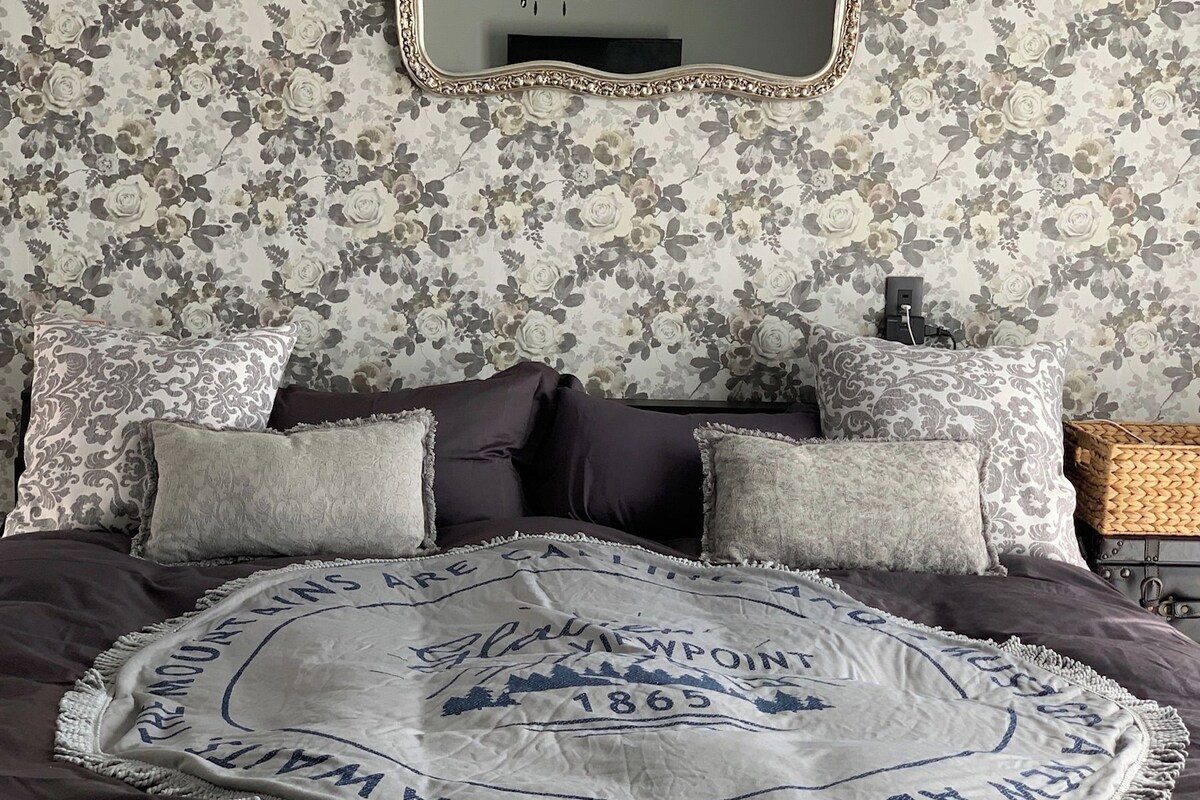 A bedroom with a floral wallpaper, a round bed with a blanket, and a mirror above the bed.