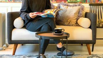 A person sitting on a sofa with a book and a cup on a small table beside them.
