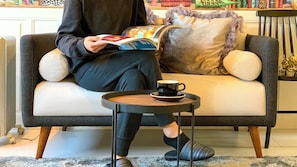 A person sitting on a sofa with a book and a cup on a small table beside them. - Sparky's House / House II (Naoshima)