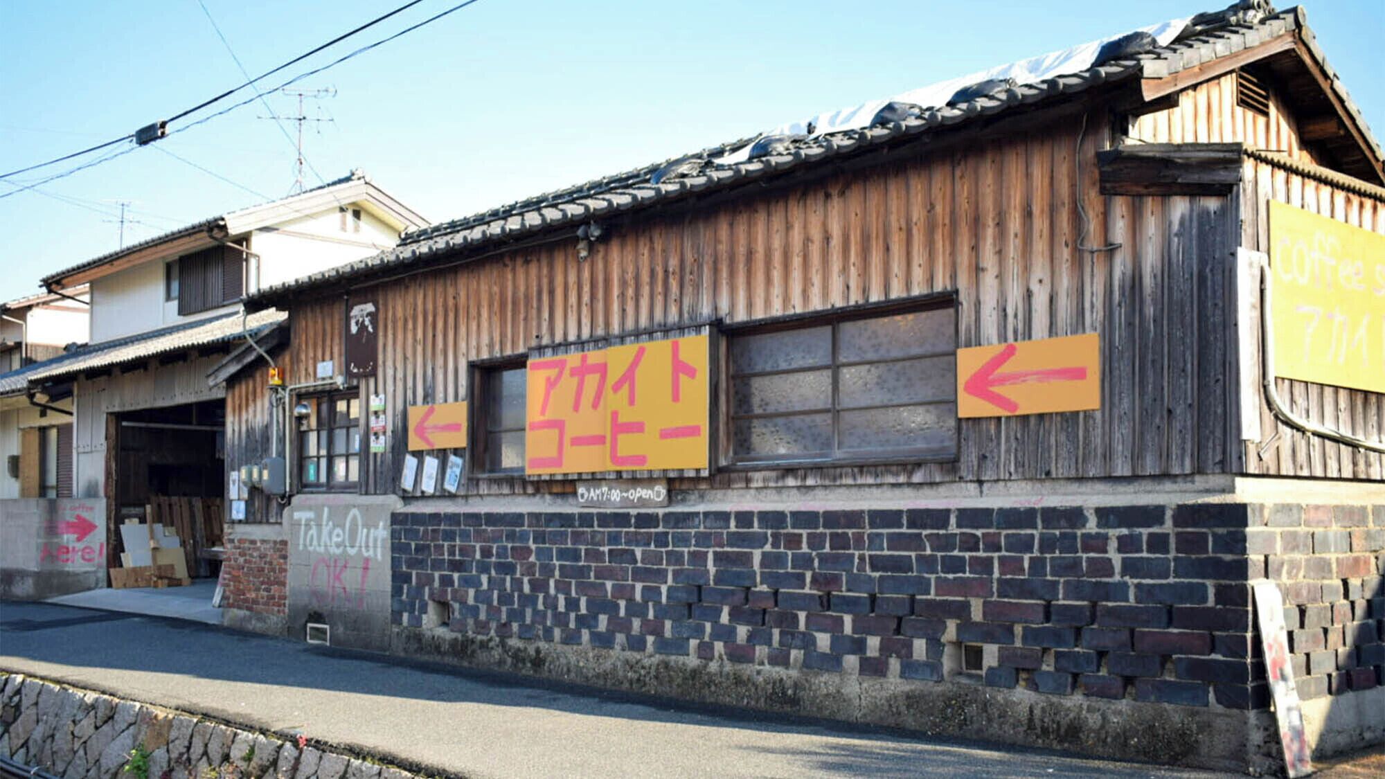 A rustic building with a wooden facade, a brick base, and signs indicating a cafe and a takeaway service.