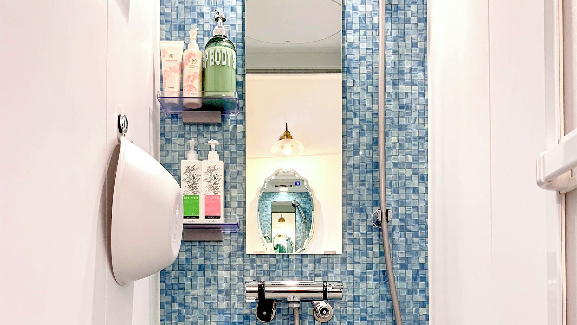 Een badkamer met een blauwe mozaïektegelwand, een spiegel, een douche met een handdouche en diverse toiletartikelen op een plank.
