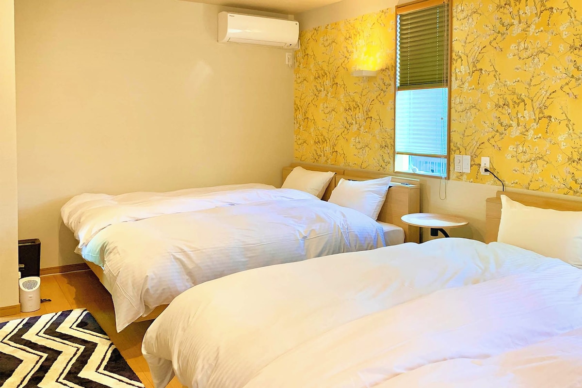 A hotel room with two single beds, a small round table, and a window with blinds.