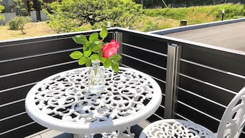 A white metal table with a glass vase and a pink rose on a balcony with a black railing.