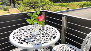 A white metal table with a glass vase and a pink rose on a balcony with a black railing. - Sparky's House / House II (Naoshima)