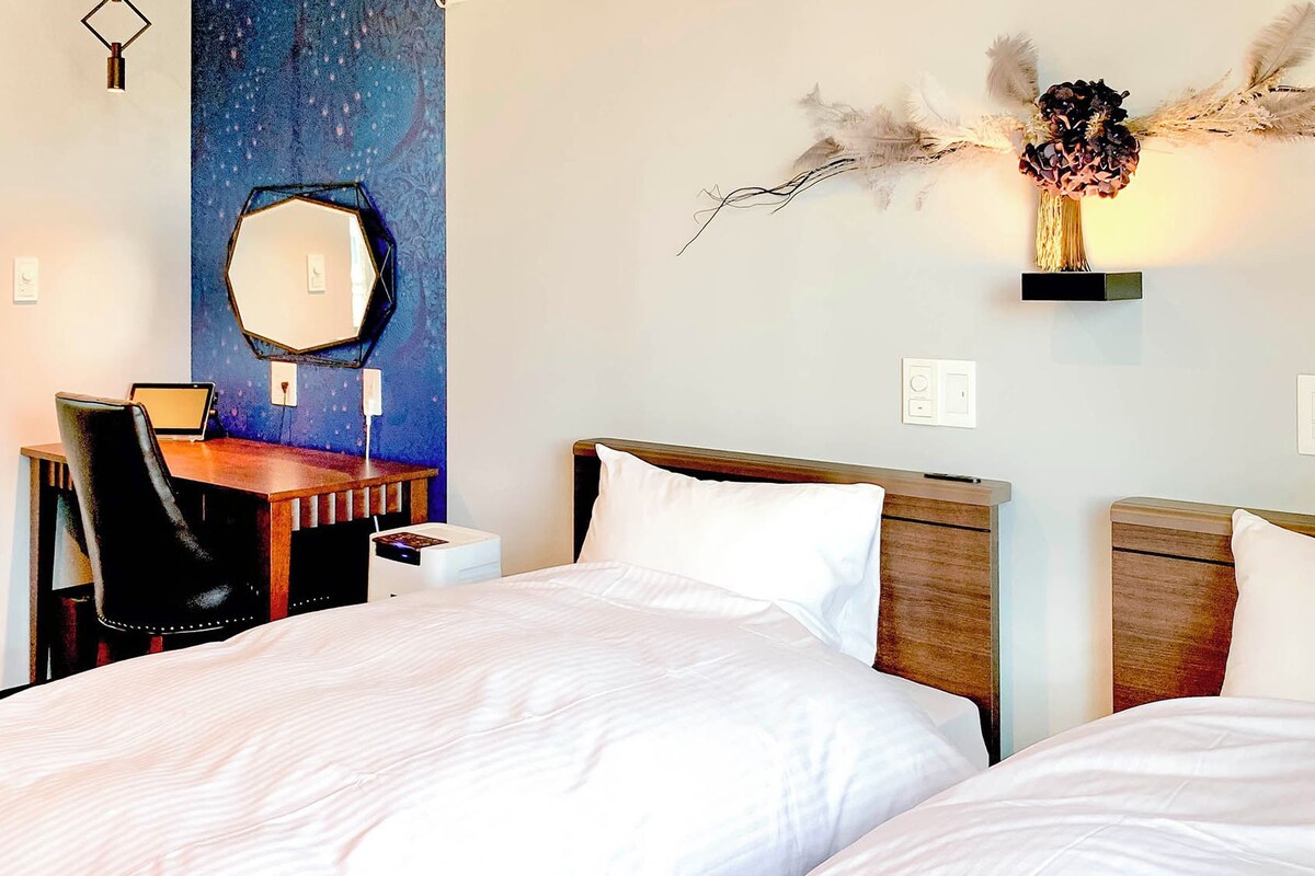 Habitación de hotel con una cama grande, un escritorio con silla, un espejo y un elemento decorativo en la pared.