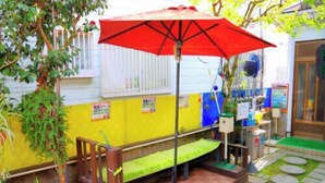 A small outdoor seating area with a red umbrella, a bench, and a planter with green plants. - Maruhei Minshuku (Tateyama)